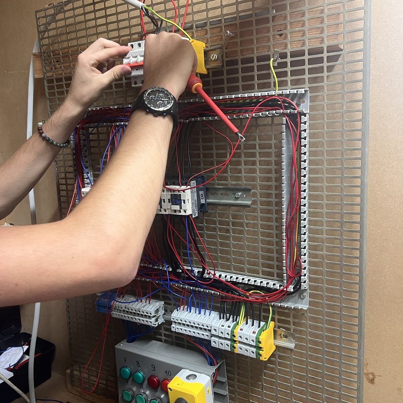 Les mains d’un élève câblent un tableau électrique en atelier