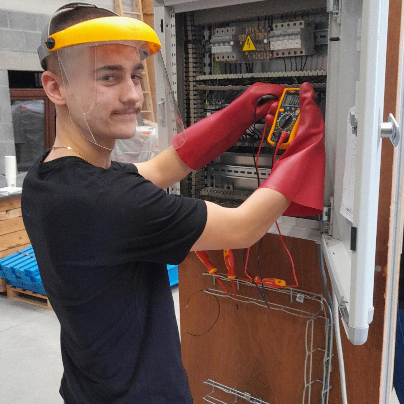 Élève avec visière et gants isolants mesurant dans une armoire électrique