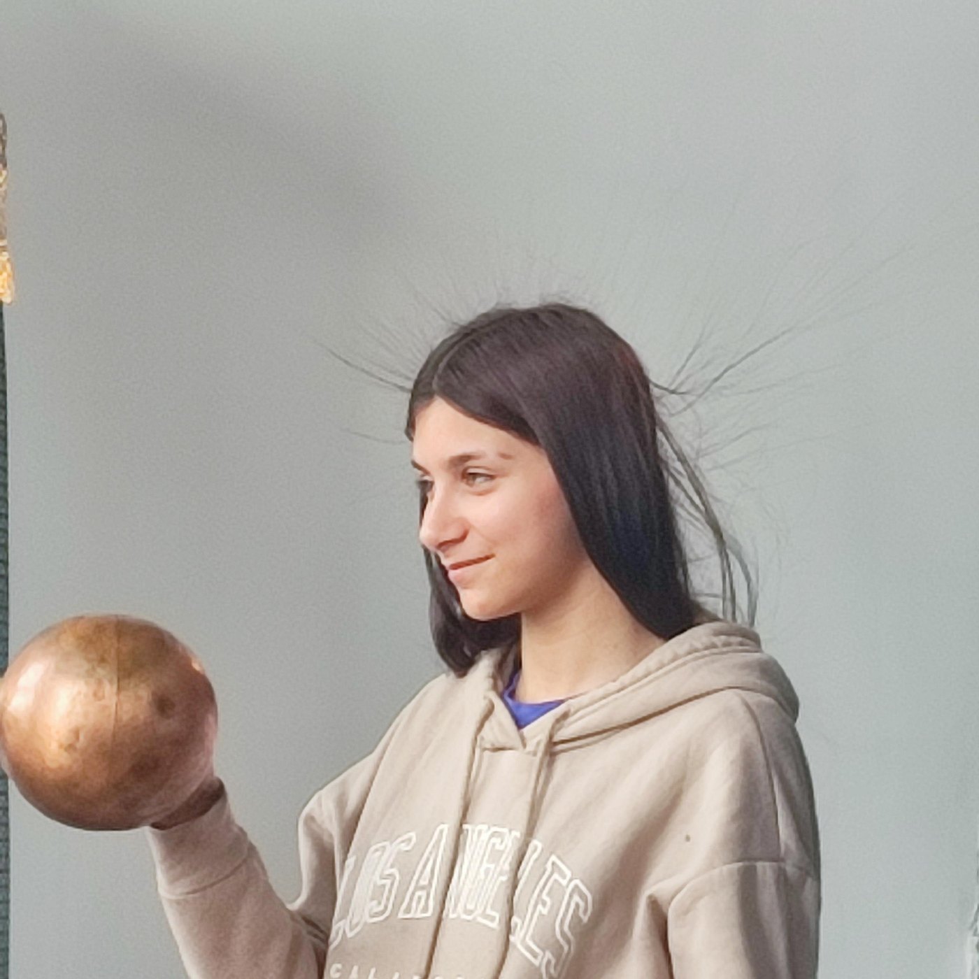 Élève la main sur un générateur électrostatique, cheveux dressés, à la Maison de la Science