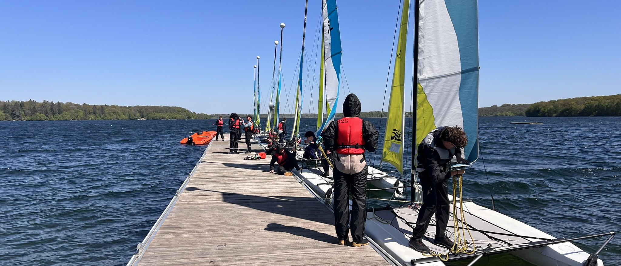 Élèves en gilet de sauvetage sur le ponton, catamarans prêts au départ pendant le stage de voile