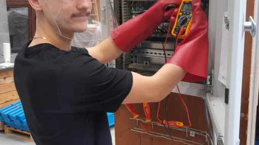 Élève avec visière et gants isolants mesurant dans une armoire électrique