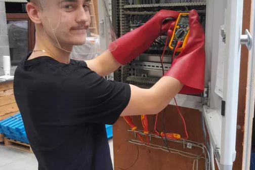 Élève avec visière et gants isolants mesurant dans une armoire électrique